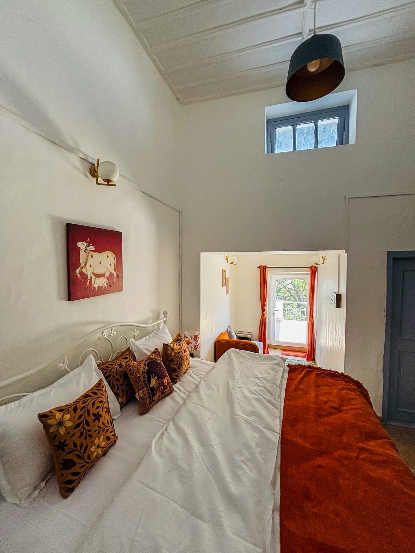 Room 02 at Shail Shikhar: a cow-and-calf Pichwai over the bed, a saffron throw, the door open to a sitting nook